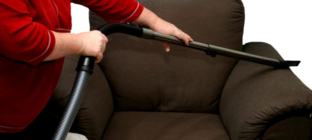 old lady cleaning cleaning the sofa using a vacuum
